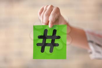 Female hand holding sheet of paper with hashtag sign on blurred background�