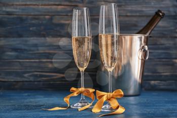 Glasses of champagne with golden bows on color wooden table�