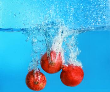 Falling of pomegranates into water on color background�