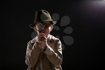 Cute little detective with magnifying glass on dark background�