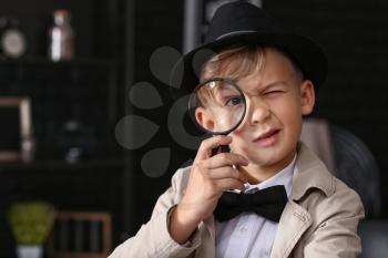 Cute little detective with magnifying glass indoors�
