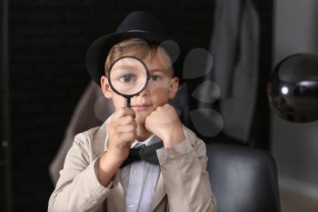 Cute little detective with magnifying glass indoors�