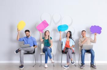Young people with blank speech bubbles sitting near white wall�