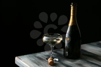Glass and bottle of champagne on wooden table against dark background�