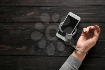 Female hand in handcuffs with mobile phone on wooden background. Concept of addiction�