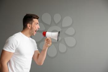 Screaming young man with megaphone on grey background�