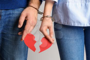 Couple with handcuffed together hands holding broken heart on light background. Concept of addiction�