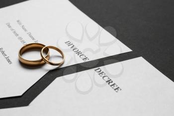 Torn divorce decree with rings on dark background�