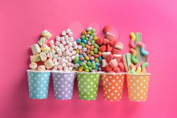 Paper cups with tasty candies on color background�