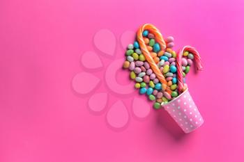 Paper cup with tasty candies on color background�