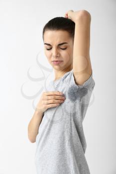 Young woman with wet spot on clothes under armpit against white background. Concept of using deodorant�