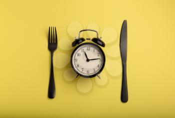 Alarm clock and cutlery on color background. Diet concept�