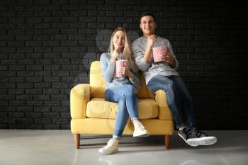 Young couple with popcorn watching movie near dark brick wall�