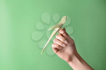 Female hand with origami parrot on color background�