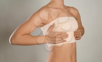 Woman with bandage on her chest against grey background. Breast augmentation concept�