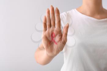Woman with pink ribbon drawn on her palm against light background. Breast cancer awareness concept�