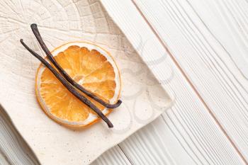 Plate with dry orange slice and aromatic vanilla sticks on white wooden background�