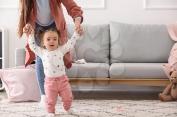 Young woman teaching her cute little daughter to walk at home�