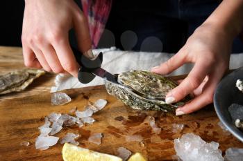 Woman opening raw oyster with knife at table, closeup�