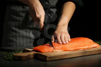 Woman cutting fillet of fresh salmon at table�
