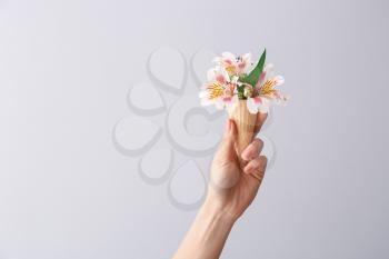 Female hand holding waffle cone with beautiful flowers on light background�
