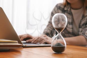 Hourglass on table of woman working with laptop. Deadline concept�