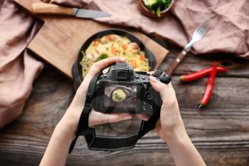 Young woman taking picture of food on wooden table�