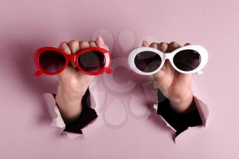 Female hands with stylish sunglasses on color background�