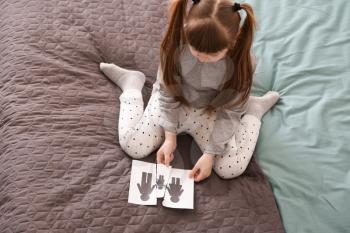 Sad little girl with torn picture of family sitting on bed. Concept of divorce�