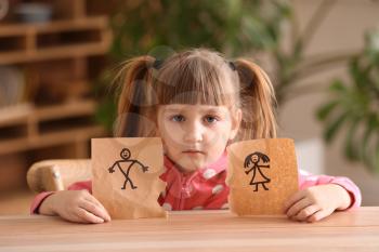 Sad little girl with torn drawing of family at table. Concept of divorce�