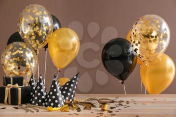 Balloons, gifts and party hats on table against color background�