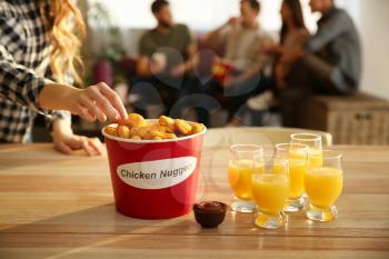 Woman taking tasty nuggets from bucket on table�