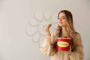 Young woman with bucket of tasty nuggets on light background�