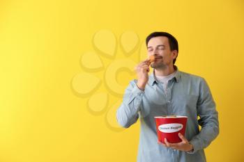 Handsome man with bucket of tasty nuggets on color background�