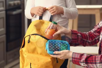 Mother putting lunch box into backpack of her little son before school�
