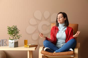 Young woman meditating in armchair at home�