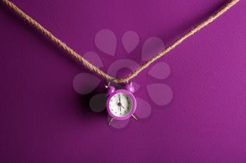 Alarm clock on rope against color background�