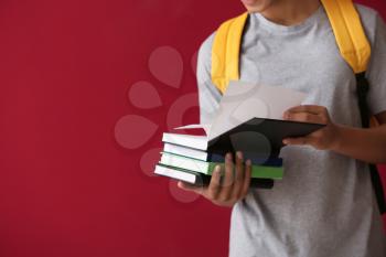 African-American schoolboy with books on color background�