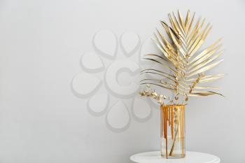 Vase with golden tropical leaf on table against light background�