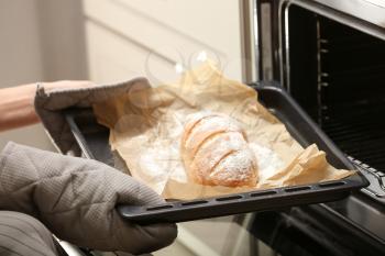 Taking of baking tray with homemade bread out of oven�