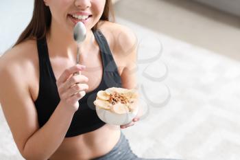 Sporty woman eating tasty yogurt at home�