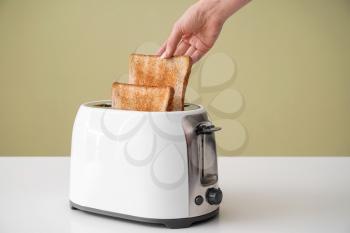 Woman taking bread slice from toaster on table�