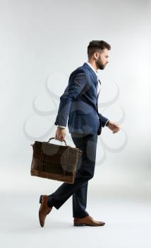 Fashionable young man in formal clothes and with bag walking against light background�