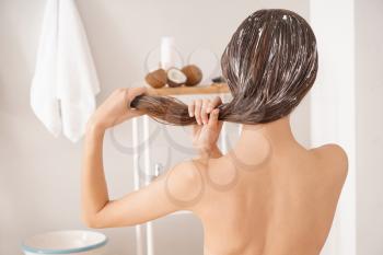 Woman using coconut oil for hair in bathroom�