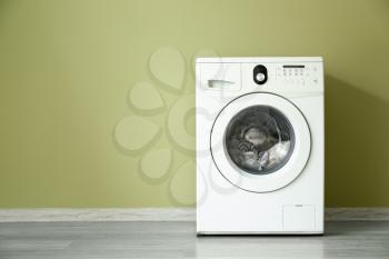 Modern washing machine near color wall�