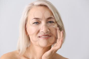 Mature woman applying face serum on light background�