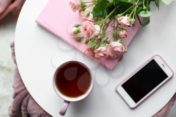 Cup of hot tea with mobile phone, flowers and book on white table�