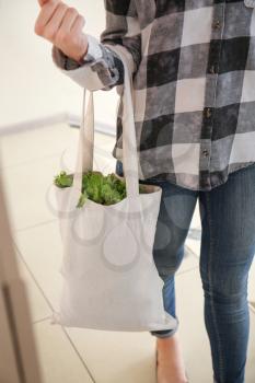 Young woman with fresh vegetables in eco bag indoors�