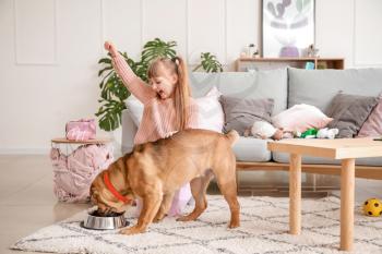 Cute little girl feeding funny dog at home�