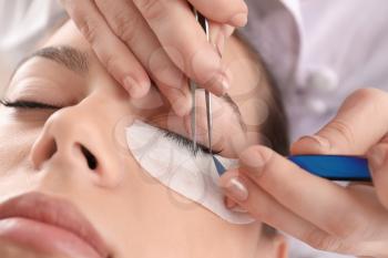 Young woman undergoing eyelash extension procedure in beauty salon, closeup�